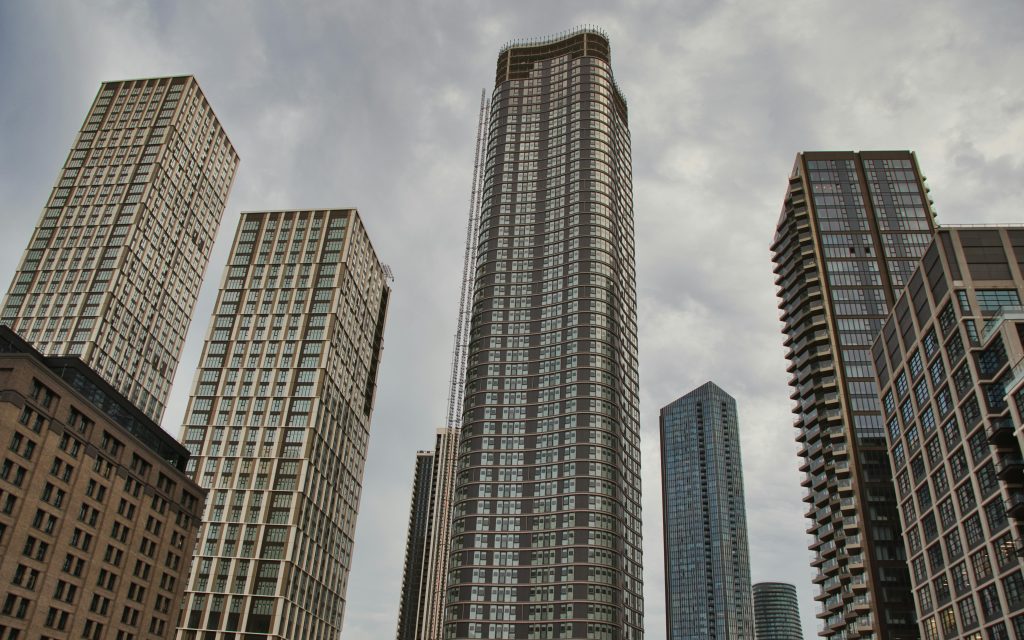 Picture of around 10 high rise buildings photographed from worm's eye view upward. The buildings appear to be office blocks in a commercial region, and are looming towards a grey sky. The image conveys a sense of corporate density.