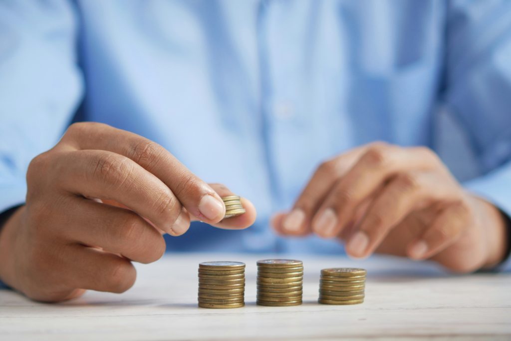 Close up of a person's hands stacking coins. The coins are a copper or brass color, and the person is wearing a blue shirt. Their torso is out of focus.